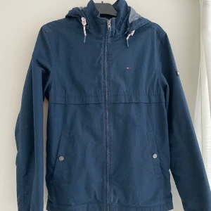 Tommy Hilfiger jacka - Jacka i nyskick från Tommy Hilfiger. Luvan är avtagbar med knappar. En perfekt jacka för våren.