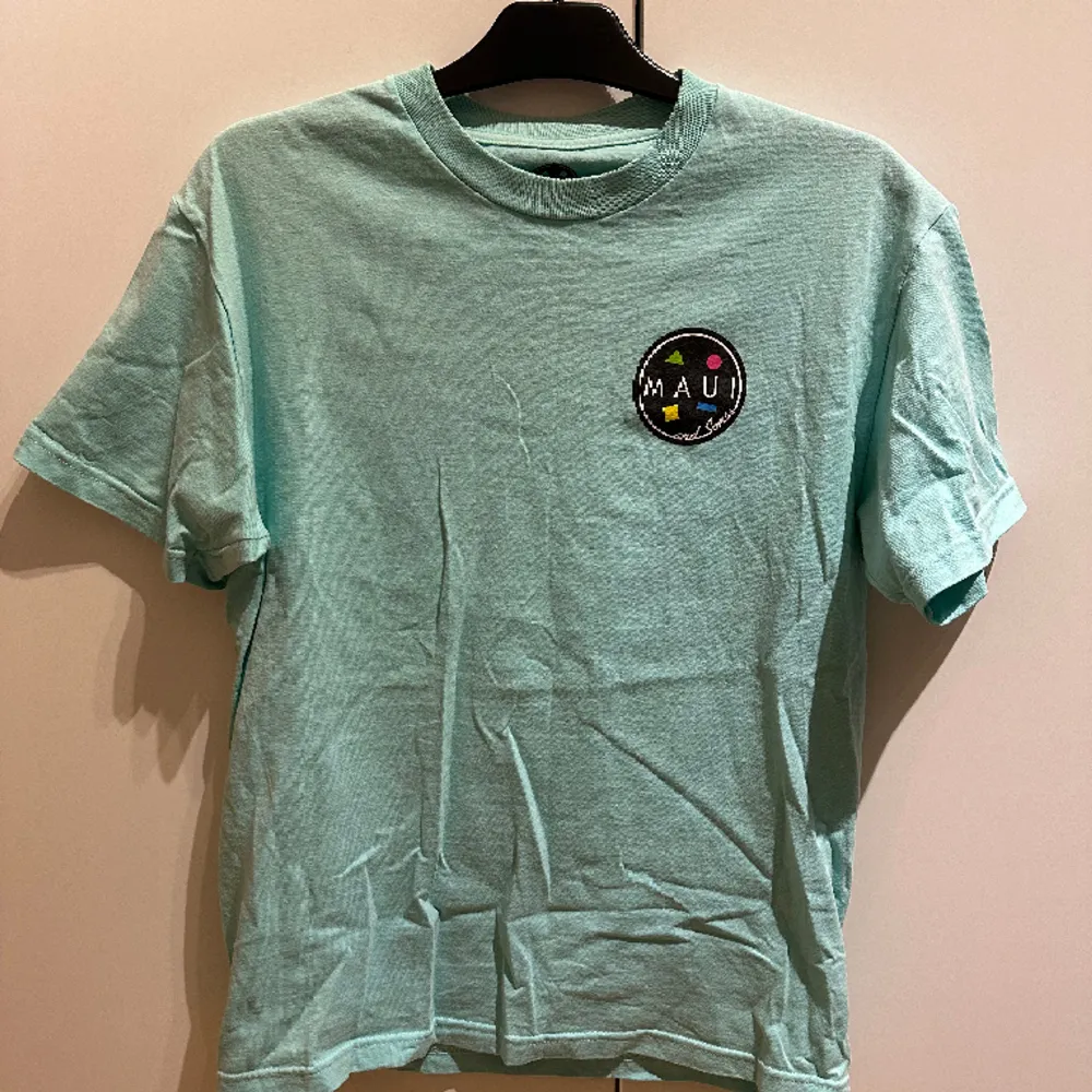 Säljer en turkos T-shirt från Maui And Sons med ett stort tryck på ryggen. Ganska oanvänd och väldigt bra skick. Ganska baggy stil. Gjord av 100% bomull och designad i Californien. . T-shirts.