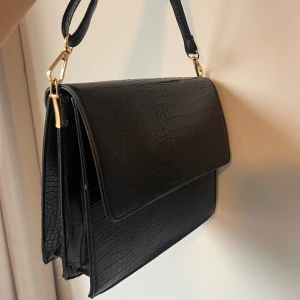 Svart axelremsväska - Säljer en svart och rymlig axelremsväska med croc mönster 🖤 helt ny och aldrig använd. Perfekt till vardags men också till fest och andra tillställningar 🪩