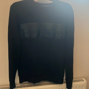 Svart tröja från Calvin Klein - En stilren svart tröja från Calvin Klein med långärmad design. Tröjan har en diskret logotyp på bröstet och är tillverkad i ett bekvämt material. Flitigt använd men i bra skick. 