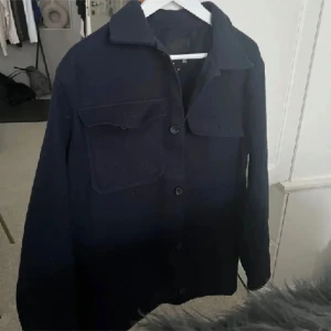 Svart overshirt - En svart overshirt med långa ärmar och knappar framtill. Jackan har två bröstfickor med lock och en klassisk krage.