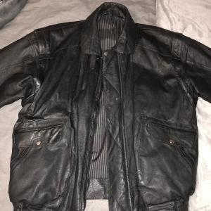 Svart skinnjacka - En svart skinnjacka med långa ärmar och två stora fickor framtill. Den är i välanvänt skick med en reva på ena ärmen. Strl 54 aka väldigt stor o baggy :) 100% äkta läder, om du vill ha fler bilder eller frågor skriv bara <3