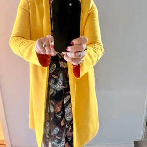 Tunn knapplös kappa - En snygg och sparsamt använd kappa i senapsgult. Jackan är i en rak modell. Tvättas för hand.