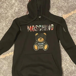 MOSCHINO hoodie - Hej! Säljer min MOSCHINO hoodie i storlek S, säljs pågrund av att jag knappt använder den och den ligger för det mesta bara i garderoben och tar upp plats.  Använd ett fåtal gånger och är köpt i England för ungefär 2 månader sedan för 4500kr