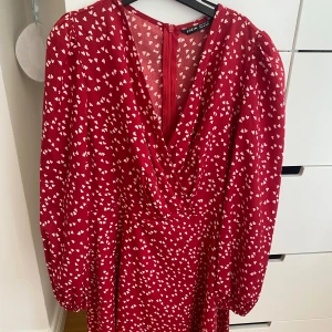 Röd klänning med hjärtan - Här är en fin röd klänning med vita hjärtan. Den här varan har används en gång vid skolavslutning så är i fint skick. Det är storlek S. Om man inte vill ha klänningen så v-ringad går det lätt att använda en säkerhetsnål. 