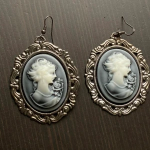 Kamé örhängen, cameo, silver, retro, vintage, romantiken, viktoriansk - Större örhängen med kaméer i grått & vitt, metalldelarna har gunmetal finish. Baksidorna har blivit missfärgade. Mått (utan krok): 6x4,5 cm.
