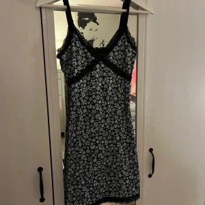 Blommig klänning - En kort figursydd klänning med blommor och spetsdetaljer upptill och nedtill samt en rosett framtill. Från H&M i strl XS!