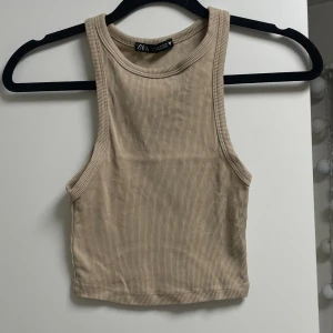 Ribbad topp - ZARA - Ribbad topp från Zara i storlek S, färgen ser lite mörk ut i första bilden, den är beige som andra bilden. Superskön material perfekt för sommaren! Nypris: 199kr