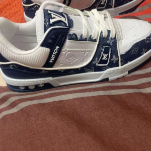 Snygga sneakers från Louis Vuitton - Säljer ett par riktigt snygga sneakers från Louis Vuitton. De är vita och blå med det klassiska LV-mönstret. Skorna har snörning och är i nyskick. Perfekta för både vardag och fest!