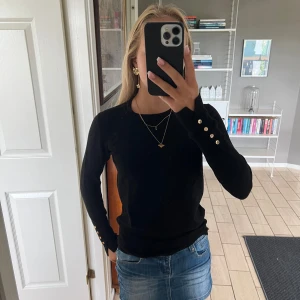 Svart tröja med guldknappar - Säljer en snygg svart tröja med långa ärmar och guldknappar vid ärmsluten. Perfekt för både vardag och fest. Tröjan är i bra skick och passar till det mesta. Köp direkt eller ge prisförslag 💛