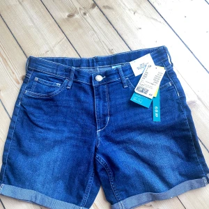 Blå jeansshorts från &Denim - Säljer ett par snygga blå jeansshorts från &Denim. De är i storlek 152 och har en klassisk femficksdesign med knapp och dragkedja fram. Shortsen har en normal passform och är perfekta för sommaren. De är i nyskick och har aldrig använts. Perfekta för både vardag och fest!