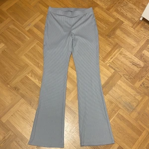 Grå randiga byxor från H&M Divided - Säljer ett par grå randiga byxor från H&M Divided i storlek M. Byxorna är högmidjade och har en bootcut-stil som ger en snygg siluett. De är tillverkade i polyester vilket gör dem bekväma och stretchiga. Perfekta för både vardag och fest! Aldrig använt då byxorna är för stora. Köparen står för frakten!