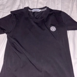Svart t-shirt från Stone Island - Säljer en snygg svart t-shirt från Stone Island. Den är i bra skick och har en broderad logga på bröstet. Perfekt för vardagsbruk eller att ha på fest. Passar till allt och är superbekväm!
