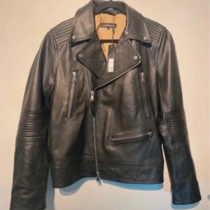 Svart skinnjacka från J Lindeberg  - Säljer en snygg svart skinnjacka från J Lindeberg. Jackan har en cool bikerstil med dragkedjor och detaljer på axlarna och ärmarna. Den är i nyskick och passar perfekt för höst och vår. Jackan har en normal passform och är gjord av högkvalitativt skinn.