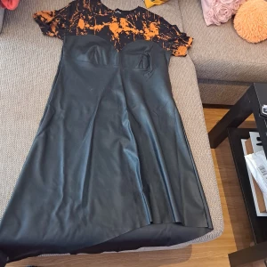 Svart och orange klänning - Säljer en snygg svart och orange klänning. Den har en cool design med en svart kjoldel och en orange och svart mönstrad överdel. Klänningen är kortärmad och har en tight passform upptill med en utsvängd kjol. Perfekt för fest eller en utekväll! 🖤🧡 