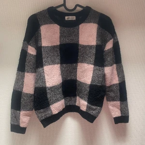 Rutig tröja från H&M - En bekväm rutig tröja från H&M med ett mönster i svart, grått och rosa. Tröjan har långa ärmar och ribbstickade muddar vid ärmslut och nederkant.