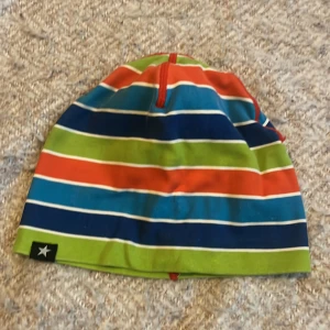Randig mössa med färgglada ränder - En färgglad mössa med ränder i blått, grönt, rött och vitt. Mössan har en liten etikett med en stjärna på kanten.