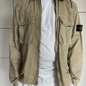 Stone Island jacka - Mycket fin jacka i nyskick. Beige med 2 bröstfickor fram. Bomull. Ofodrad.  Storlek L, modellen på bilden är 183cm. Säljes för 2500kr, nypris 4900kr.