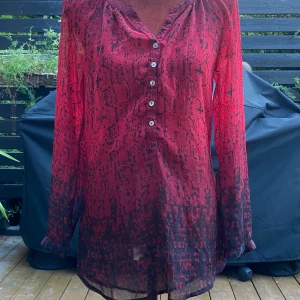 Röd/svart blus Street One 36 - Röd/svart blus med knappar i urringning och ärmslut. Längd: 73 cm Axelbredd: 44 cm  Katter finns i hemmet!