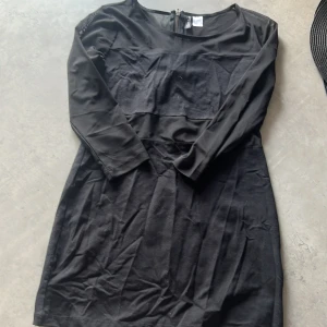 Svart klänning från H&M Divided - En elegant svart klänning från H&M Divided med trekvartsärm och dragkedja i ryggen. Klänningen har en transparent mesh-detalj på ärmarna och övre delen av ryggen.