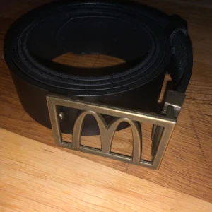 McDonald’s Bälte - Säljer mitt McDonalds-bälte. Det har den Klassiska gyllene bågen på spännet och är en rolig accessoar för alla McDonalds-fans som vill lägga en annorlunda touch till din outfit.