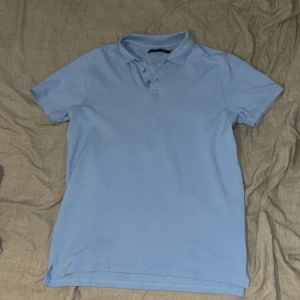 Ljusblå pikétröja - En ljusblå pikétröja med korta ärmar och en klassisk krage med knappar. Tröjan är tillverkad i ett bekvämt material och har en normal passform.