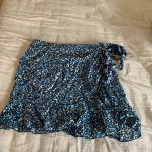 Minikjol - Super gullig blommig mini kjol med knytning på sidan och lite volanger!!