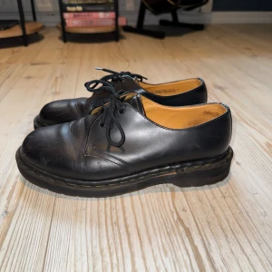 Dr. Martens 1461 - Dr. Martens i modell 1461. Köpta second hand. Tror sömmen ska vara gul men att personen innan har putsat över den så ser nästan svart ut. Behövs förmodligen putsas igen då de inte är jätteglansiga. Annars väldigt fint skick, endast lite creasade!🖤💛
