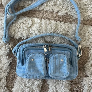 Núnoo väska - Helena Terry light blue Núnoo väska💕 Mått: 10*17.5*4 (höjd*bredd*djup). Kommer med axelrem som kan tas av. Endast använt en gång, nypris 1050kr 