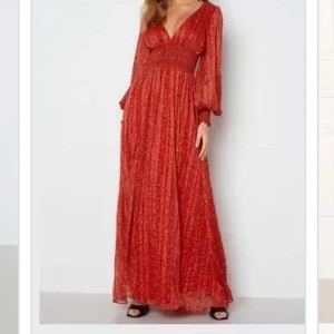Goddiva Maxi klänning  - Helt ny, röd Goddiva klänning med små blommor och guldtrådar. Har kvar märkeslappen. V-ringad fram och i ryggen. Långärmad med smock i ärmslutet och midja. Väldigt fin klänning! 