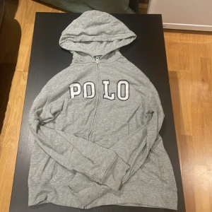 Polo Ralph Lauren zip Hoodie - Den är i använt skick, man kan se att den är använd för det finns små ”slitningar” på tröjan, men inga stora skavanker så som hål eller att drag kedjan hackar. Tröjan passa någon som har storlek S i hoodies.