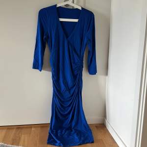 Långärmad lång klänning i härlig royal blå färg. V ringad hals som ger effekten av en längre elegant hals. Draperad wrap klänning som ger en kvinnlig siluett 