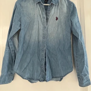 Jeansskjorta U.S. Polo  - Jättefin jenssskjorta/ jeansblus från US polo i storlek XS, ca 152-158. Skjortan är i tunn denim och hågat figursydd. Fint skick.