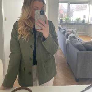 Grön vårjacka - Fin vårjacka från Kappahl med snören i midjan så man kan dra åt och göra den mer figursydd. Säljer då den aldrig kommer till användning för mig. 