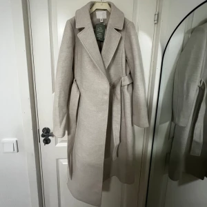 Kappa med knytskärp från HM - Storlek xxs i färgen beige, aldrig använt ordinarie pris 549kr