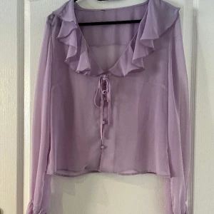 Lila blus  - En lila blus med knappar fram samt volanger 