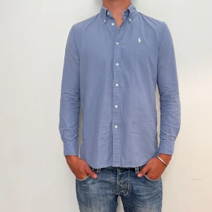 Ralph Lauren  - Blå Ralph Lauren skjorta i storlek S. Skjortan är i fint skick men har ett knappt syndlig fläck (se bild). Modellen är 186 cm lång. Orginalpris ca 1500 kr och nu endast 499