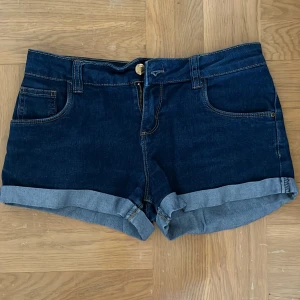 Mörkblå jeansshorts  - Ett par mörkblå jeansshorts från Denim Co. i storlek 12-13 år (158 cm). Shortsen har en klassisk femficksdesign med upprullade benslut och en knapp- och dragkedjestängning framtill.