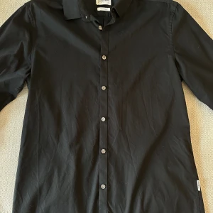 Skjorta från Lindbergh - Säljer nu min sparsamt använda skjorta från Lindbergh. Då jag är väldigt bredaxlad så vart den lite för tight för min smak, men är du en storlek M eller L men inte allt för brett axelparti lär den sitta perfekt!   Skjortan har en ytbehandling vilket 