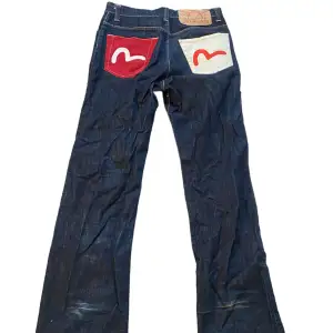 As nice baggy jeans från Evisu. Tyvärr lite slitna nertill men man tänker inte riktigt på det. Innerbenslängd: 80 cm. Ytterbenslängd: 109 cm. Midjemått mätt rakt över: 42 cm