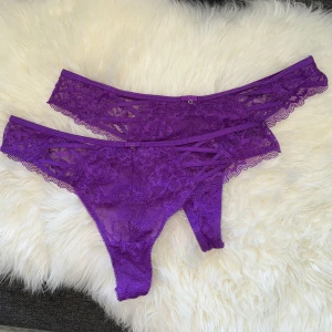 Lila stringtrosor - Lila oanvända stringtrosor med spets, snören och silvriga små hjärtan i mitten. Storlek M, kan passa S beroende på passform. Båda säljs ihop.