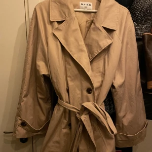 Trenchcoat kort - En kort trenchcoat köpt från NA-KD! 💚 Den är i superfint skick då den använts endast en gång. Lite större i storleken så det är något värt att tänka på. ☺️💞
