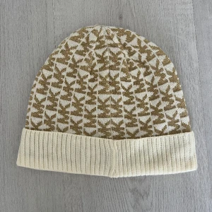 Mössa från Michael Kors - Mössa i vit & guld från MK köpt i Nyc. Använd fåtalet gånger så är i fint skick.