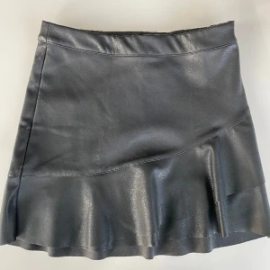 Skinnkjol tjej strlk 146 - Snygg svart Skinnkjol (ej äkta skinn) i storlek 146 från Kappahl. Snygg detalj med volang. Justerbar i midjan. Väldigt fint skick, endast använd ett par gånger. Rök- & djurfritt hem. 