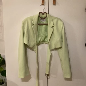 Croppad blazer - Croppad blazer i piggelin-grön färg från Angelica Blicks kollektion med nakd. Spänne som går från framsidan och fästs i ryggen. Använd 1 gång 