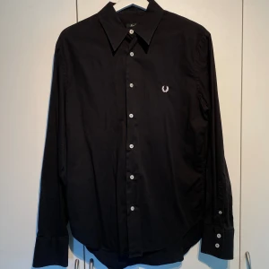 Fred Perry helsvart skjorta - Hej, säljer en helsvart skjorta från Fred Perry i använd men fortfarande okej skick. Storlek L men passar även M. Nypris 1100kr. Bekväm och skön. Pris kan diskuteras. Hör av dig i DM! 