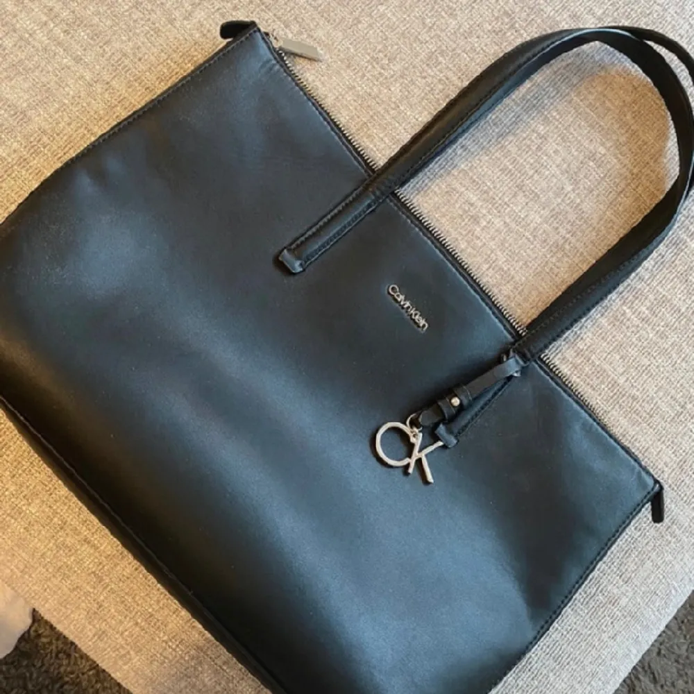 Svart handväska från Calvin Klein med tre fickor i. Inköpt i våras men använt sparsamt så i fint skick. Tygväskan som den levererades i kommer med. Nypris 1199:-. Väskor.
