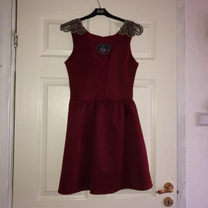  - Superfin vinröd klänning med dekorativ längs axlarna. Oanvänd. Ev frakt tillkommer 29 kr 
