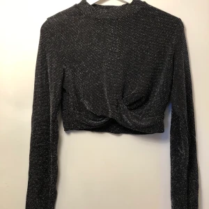 Glittrig cropptopp - Glittrig cropptopp med inbyggd knut i fram. Aldrig använd, lapp kvar. Är i ett set tillsammans med byxorna i samma glittriga mönster/färg. Hela setet 100kr.