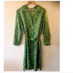 Klänning i paisleymönster - Säljer denna ljuvliga klänningen i grönt paisleymönster. Tyget är silkigt. Fint skick förutom att överste knappen är borta (se sista bilden). Den är märkt 46 men passar på mig som är storlek 40 så den passar många storlekar då det finns snöre till midjan❤